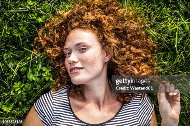 portrait of smiling young woman lying on a meadow - sommersprossen stock-fotos und bilder