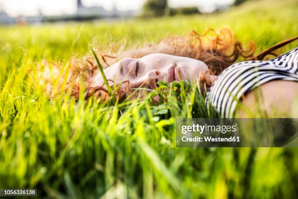 portrait of redheaded young woman with eyes closed lying on meadow - women lying stock-fotos und bilder