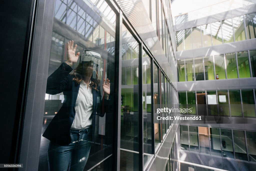 Businesswoman wearing VR goggles, standing at window