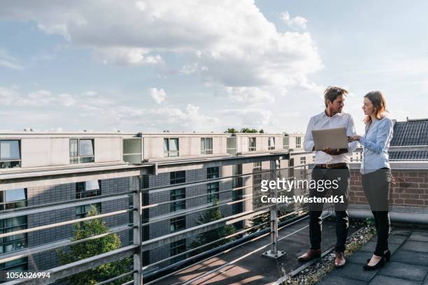 business people standing on balcony, discussing, using laptop - gespräch frau mann stock-fotos und bilder