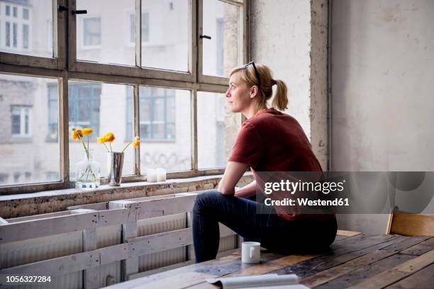 woman sitting on desk in loft looking through window - table side view stock pictures, royalty-free photos & images