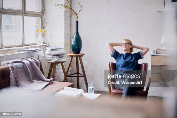 smiling woman sitting on arm chair in loft looking through window - donna poltrona foto e immagini stock