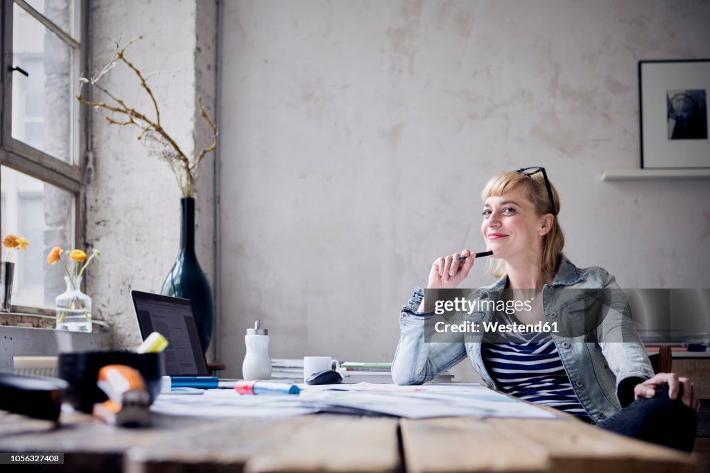 Portrait of smiling woman sitting at desk in a loft