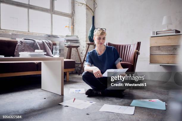 smiling woman sitting on the floor in a loft looking at papers - anrichte stock-fotos und bilder