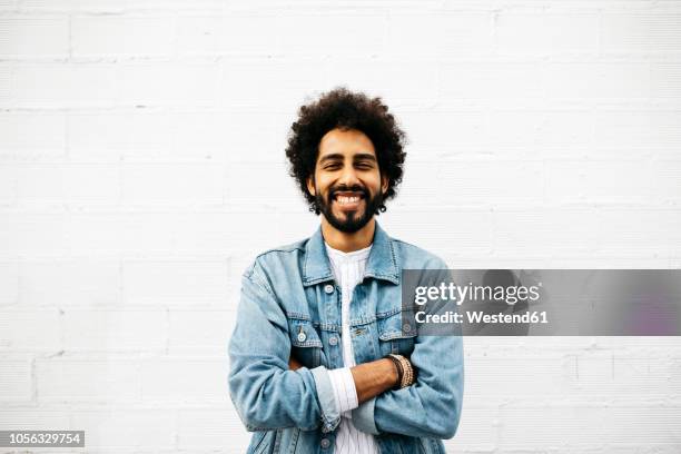 portrait of grinning young man in front of white wall - jean jacket stock-fotos und bilder