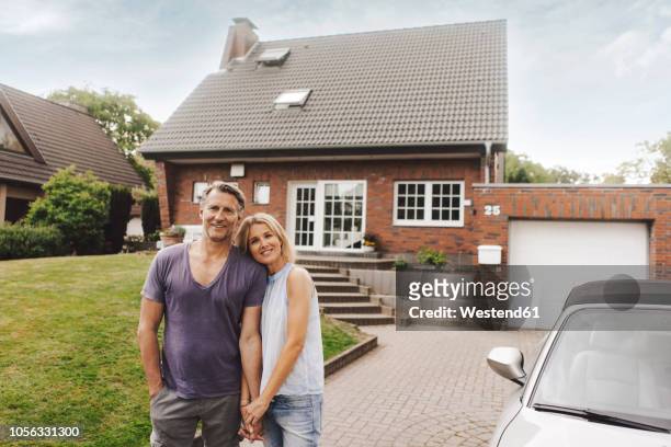 portrait of smiling mature couple standing in front of their home - garage driveway stock pictures, royalty-free photos & images