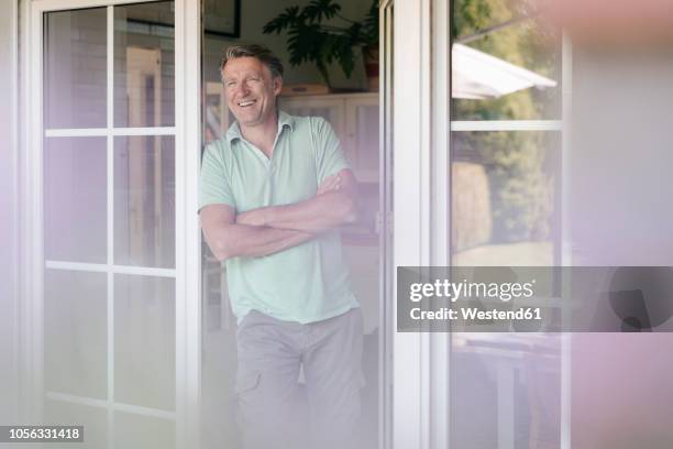 laughing mature man standing at french window - porte d'accès à la terrasse photos et images de collection