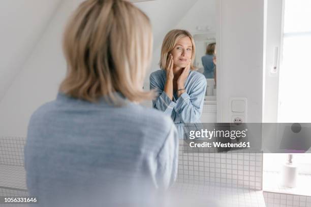mature woman looking in bathroom mirror - espejo fotografías e imágenes de stock