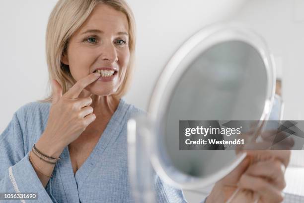 mature woman looking in beauty mirror in bathroom checking her teeth - tand stockfoto's en -beelden