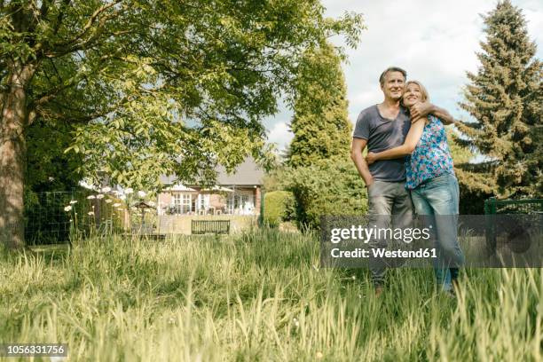 smiling mature couple embracing in garden of their home - low angle view nature stock pictures, royalty-free photos & images