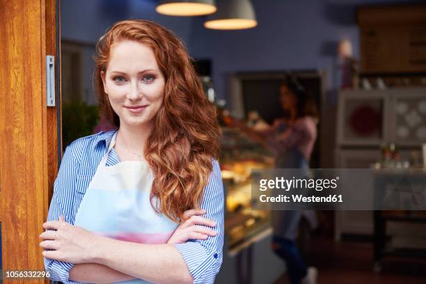 portrait of smiling young woman at the entrance of a bakery - rote haare stock-fotos und bilder