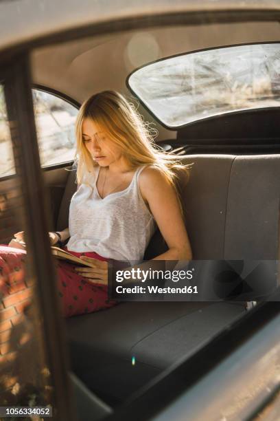 young woman sitting in a car reading book - magenta car stock pictures, royalty-free photos & images