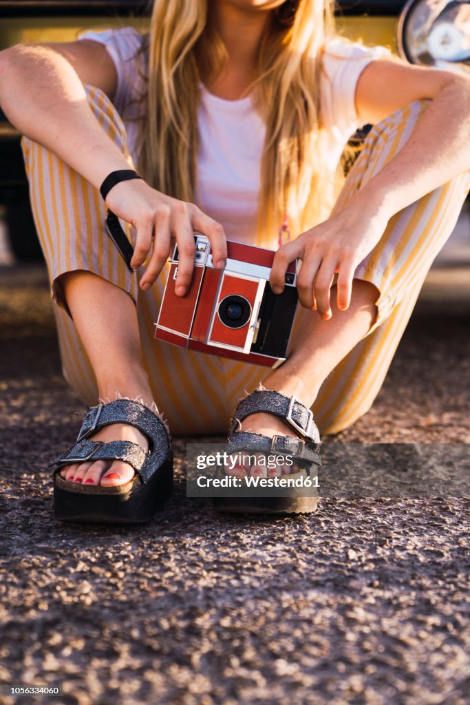 Young woman holding vintage camera sitting outside at a van