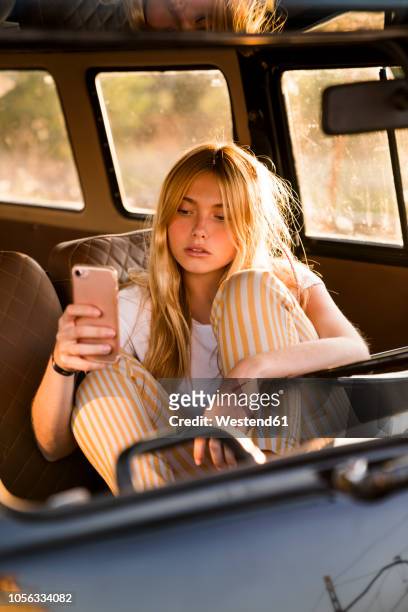 young woman sitting in a van using cell phone - blond hair young woman sunshine stockfoto's en -beelden