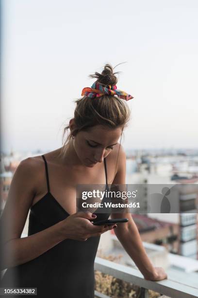 young woman wearing black dress using cell phone on balcony - dekolletage foto e immagini stock