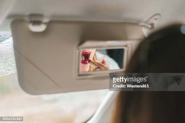 woman mirrored in rear view mirror applying red lipstick in car - woman lipstick rearview stock-fotos und bilder