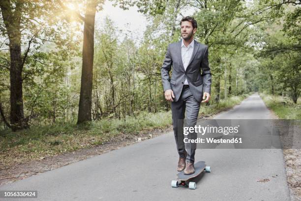 businessman riding skateboard on rural road - gray suit stock pictures, royalty-free photos & images