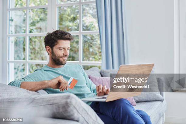 smiling man at home shopping online - mann mit kreditkarte stock-fotos und bilder
