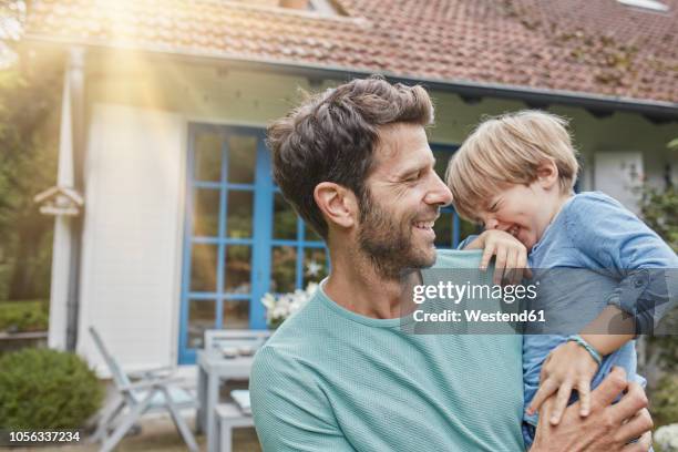 happy father carrying son in front of their home - típico de clase mediana fotografías e imágenes de stock