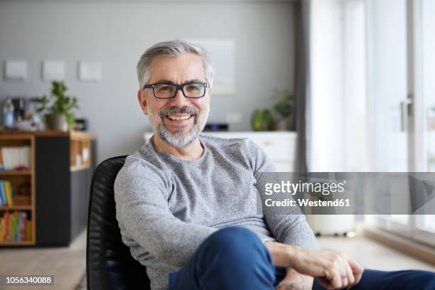 portrait of content mature man in his living room - männer über 40 stock-fotos und bilder