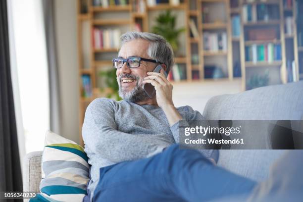 mature man on the phone sitting on couch at home looking out of window - am telefon stock-fotos und bilder