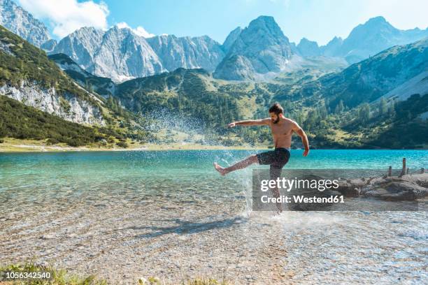 austria, tyrol, young man at lake seebensee kicking water, having fun - austria summer stock pictures, royalty-free photos & images