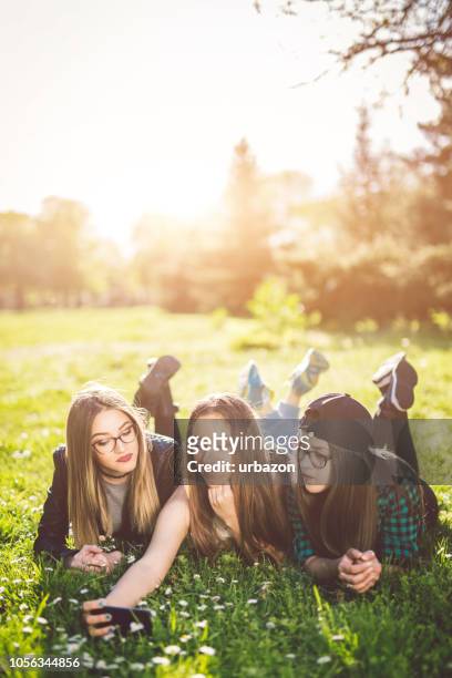three girls lying on grass taking a selfie - selfie three people stock pictures, royalty-free photos & images