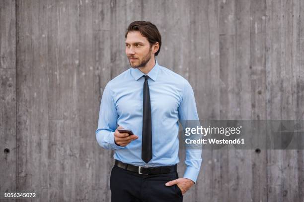 businessman standing at concrete wall holding smartphone - looking around stock pictures, royalty-free photos & images
