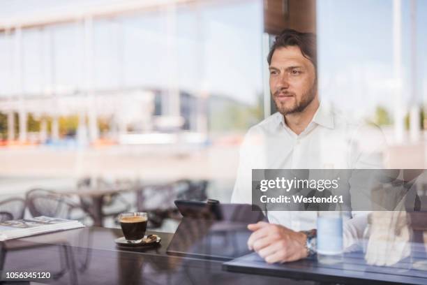 businessman behind windowpane using tablet in a cafe - un seul homme d'âge moyen photos et images de collection