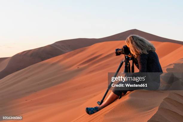 africa, namibia, namib desert, naukluft national park, female photograper photographing at early morning light, sitting on sand dune - photographer stock pictures, royalty-free photos & images