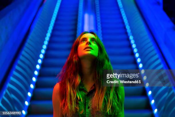 portrait of illuminated young woman in front of blue lighted escalator looking up - portrait français photos et images de collection