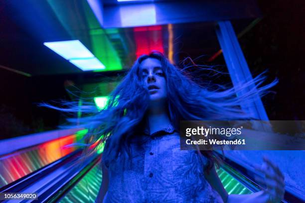 portrait of blue illuminated young woman on escalator - flatterndes haar stock-fotos und bilder