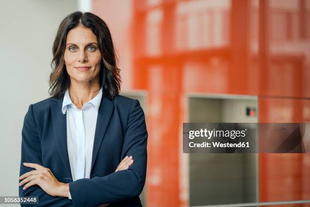 portrait of a successful businesswoman, standing in front of elevator, with arms crossed - woman in suit stock pictures, royalty-free photos & images
