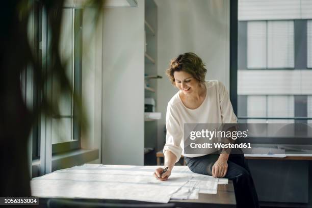 businesswoman sitting in office, working on blueprints - 2018 blueprint stock-fotos und bilder