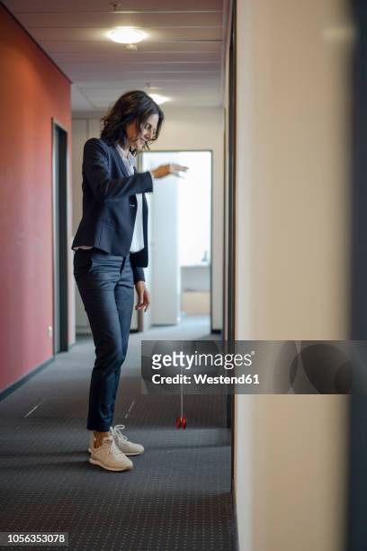 mature businesswoman standing in office corridor, playing with yoyo - jojo stockfoto's en -beelden
