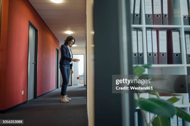 mature businesswoman standing in office corridor, playing with yoyo - jojo stockfoto's en -beelden