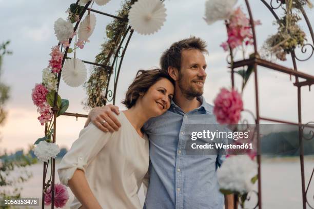 happy couple embracing under wedding arch - wedding planning stock pictures, royalty-free photos & images