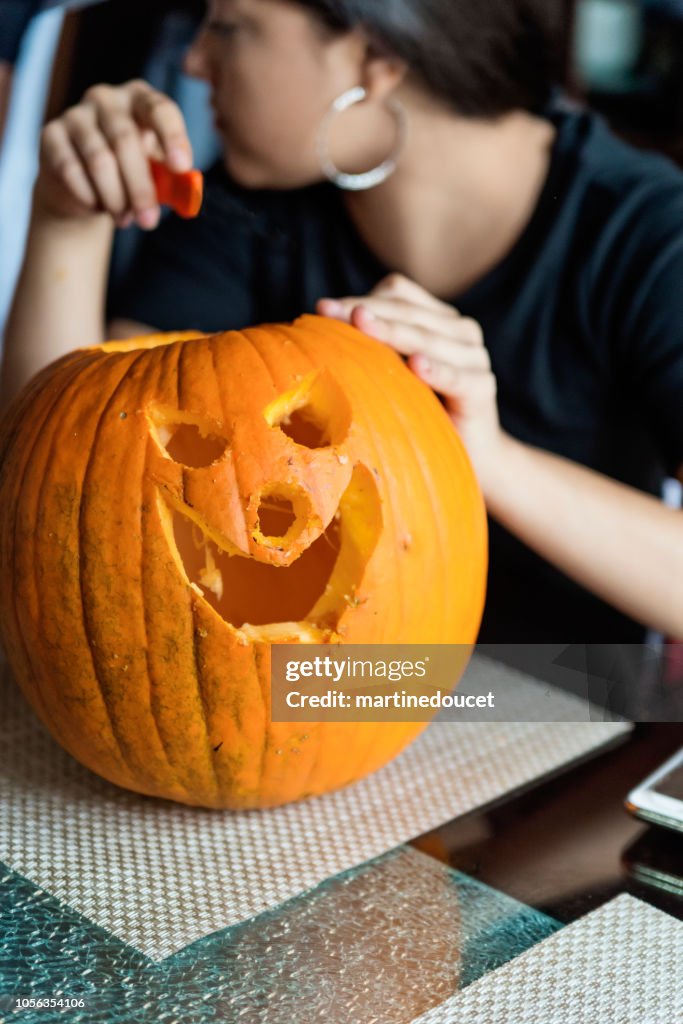 Teenage Latin American girl carving and decorating pumpkin for Halloween