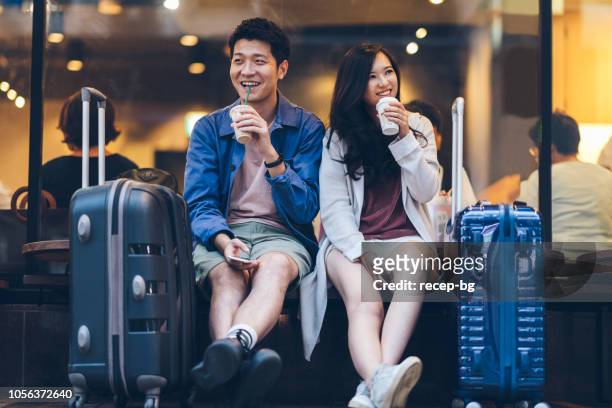 two asian tourists with suitcases spending happy time in cafe - chinese ethnicity stock pictures, royalty-free photos & images