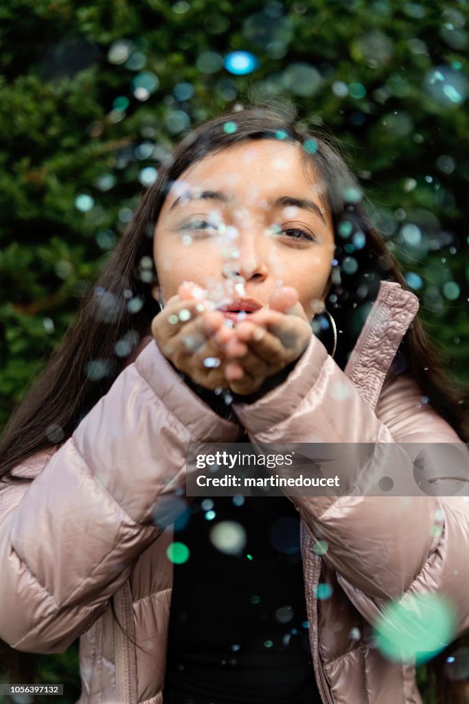 Latin American teenage girl blowing confettis outdoors.