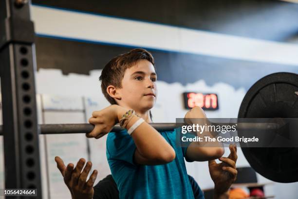 father assisting son lifting weights in gym - young kid and barbell stock-fotos und bilder