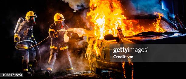 two firefighters extinguishing a burning car with foam - car flames stock pictures, royalty-free photos & images