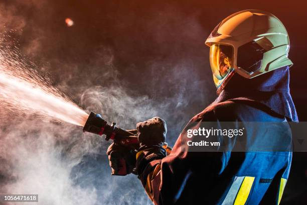 fireman operating a water fire hose - fire hose stock pictures, royalty-free photos & images