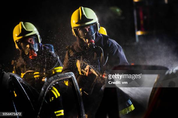 feuerwehrleute mit gasmasken sprühwasser auf fahrzeuge - firefighter's helmet stock-fotos und bilder
