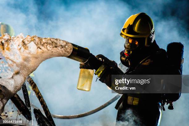 fireman extinguishing a burning car with foam - firefighter stock pictures, royalty-free photos & images