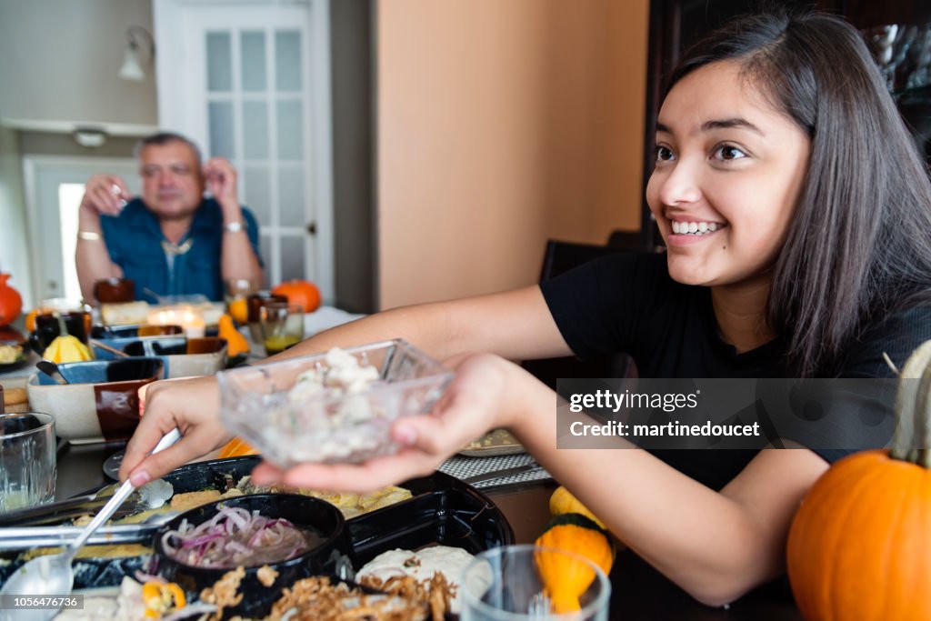 Latin American teenage girl putting food on plates at family gathering.