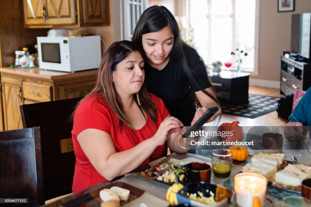 Latin American mother and teenage daughter looking at mobile phone.