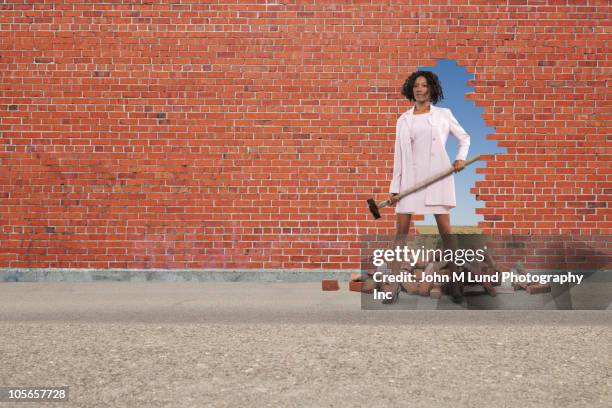 black businesswoman breaking through brick wall - sledgehammer stockfoto's en -beelden