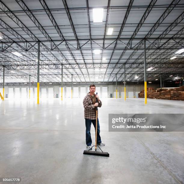 caucasian man sweeping large, empty warehouse - industrial cleaning stock pictures, royalty-free photos & images