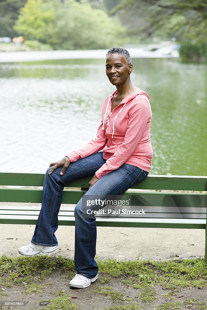 African American woman sitting on park bench near lake